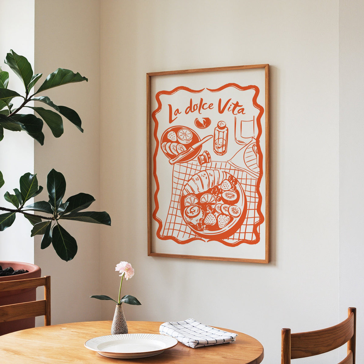 La Dolce Vita table print in a walnut frame above a round table beside a fiddle-leaf fig