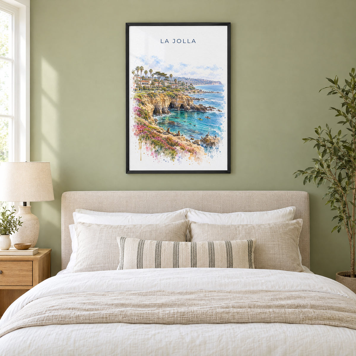 La Jolla watercolor print in a black frame above an upholstered headboard in a sage green bedroom