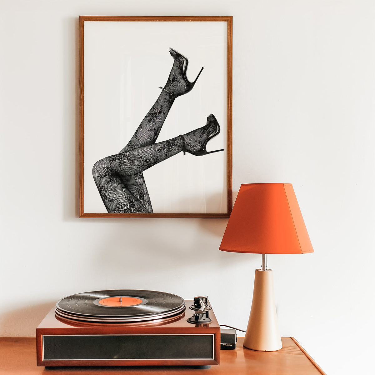 Legs in floral lace tights and stilettos print in a walnut frame above a record player and orange lamp
