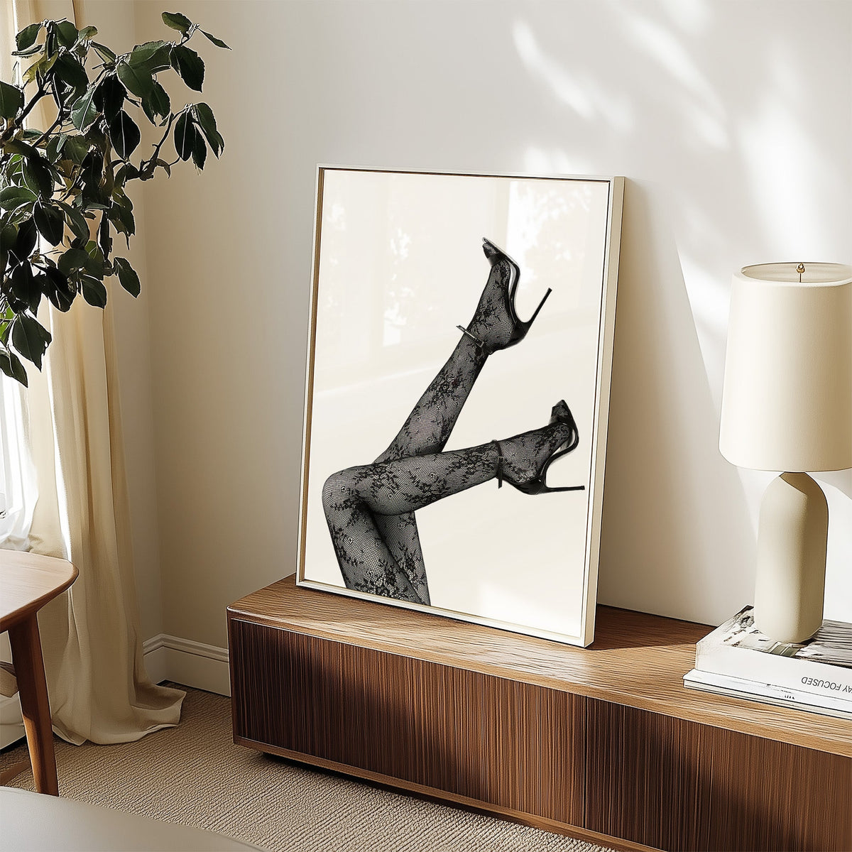 Legs in floral lace tights and stilettos print in a white frame on a walnut sideboard beside a ceramic lamp