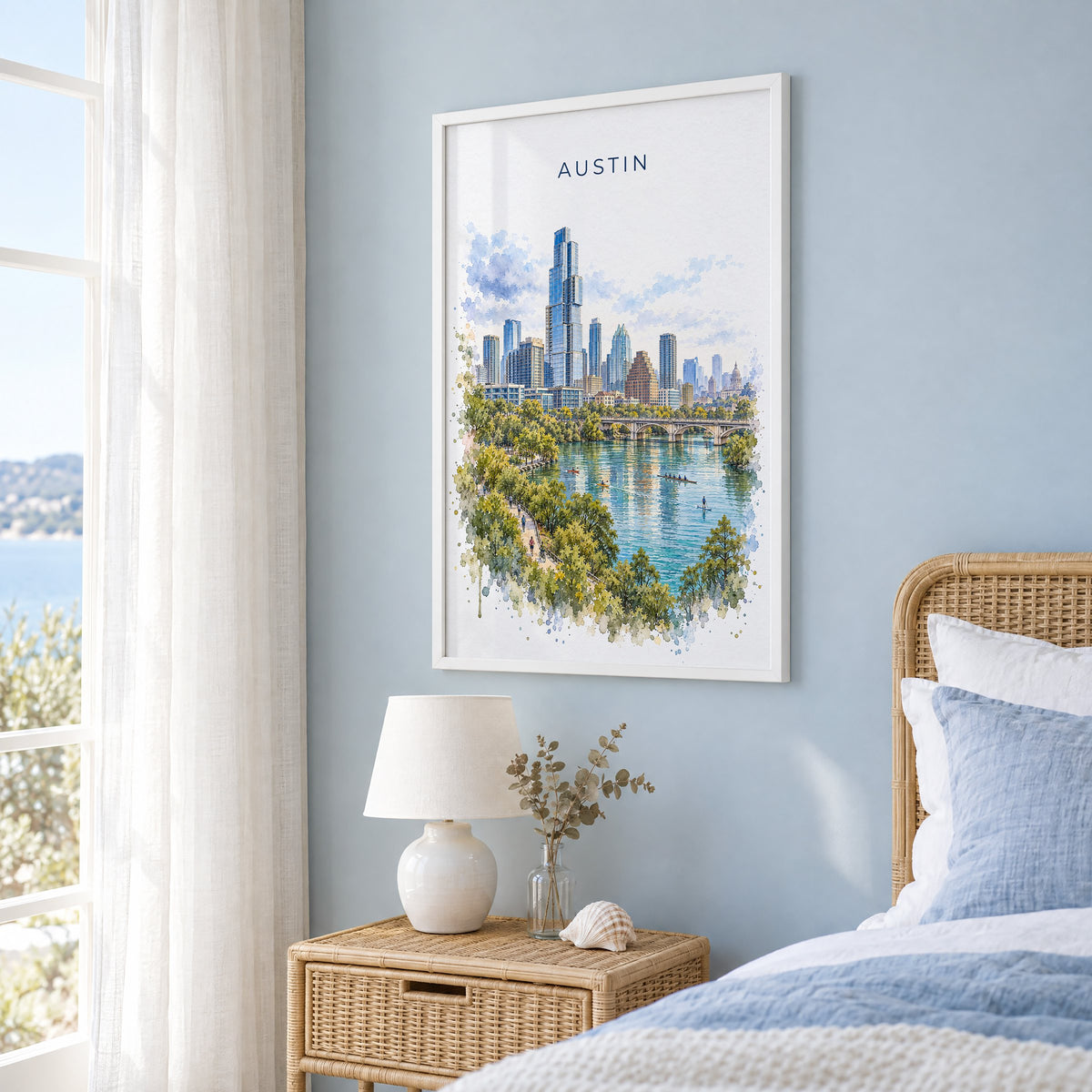 Lady Bird Lake Austin watercolor print in a white frame on a pale blue wall beside a rattan bed in a coastal bedroom