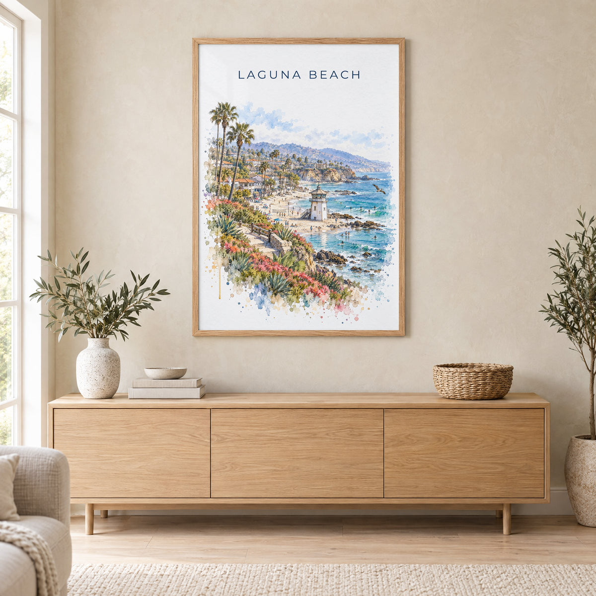 Laguna Beach watercolor print in an oak frame above a light wood sideboard in a Scandinavian living room