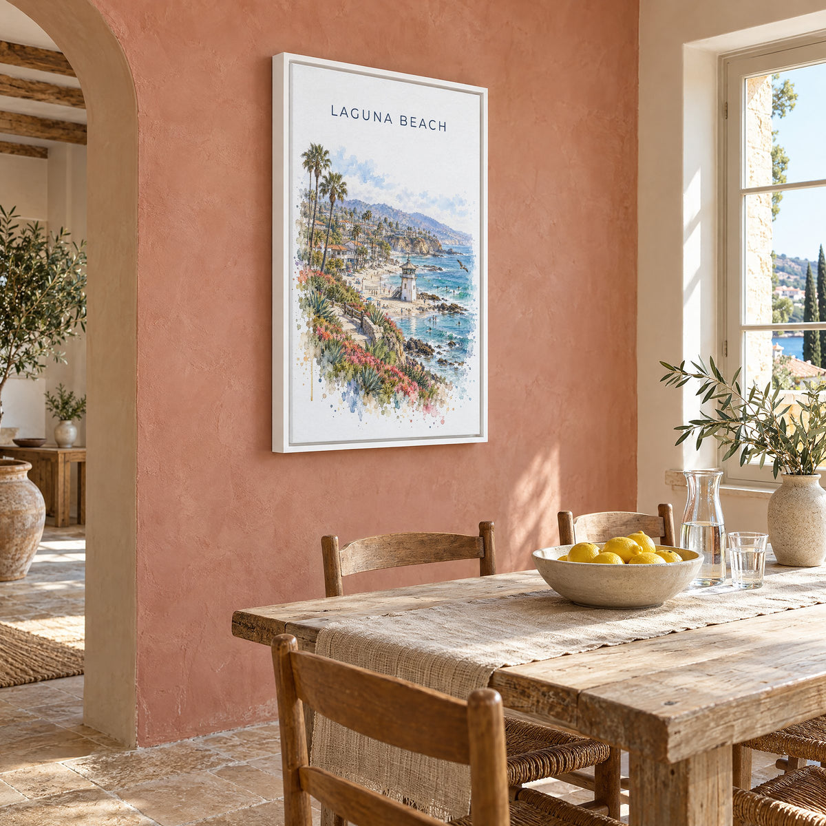 Laguna Beach watercolor print as a white floater canvas on a terracotta wall above a rustic dining table