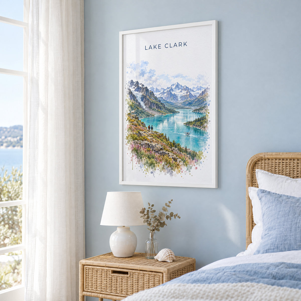 Lake Clark National Park watercolor print in a white frame on a pale blue wall beside a rattan bed in a coastal bedroom