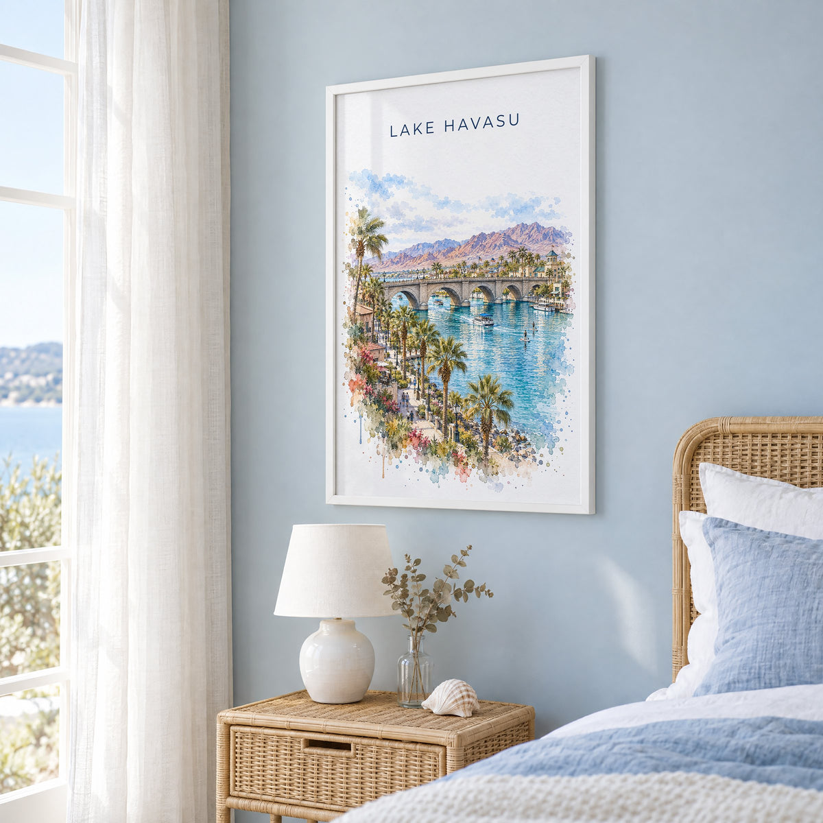 Lake Havasu watercolor print in a white frame on a pale blue wall beside a rattan bed in a coastal bedroom