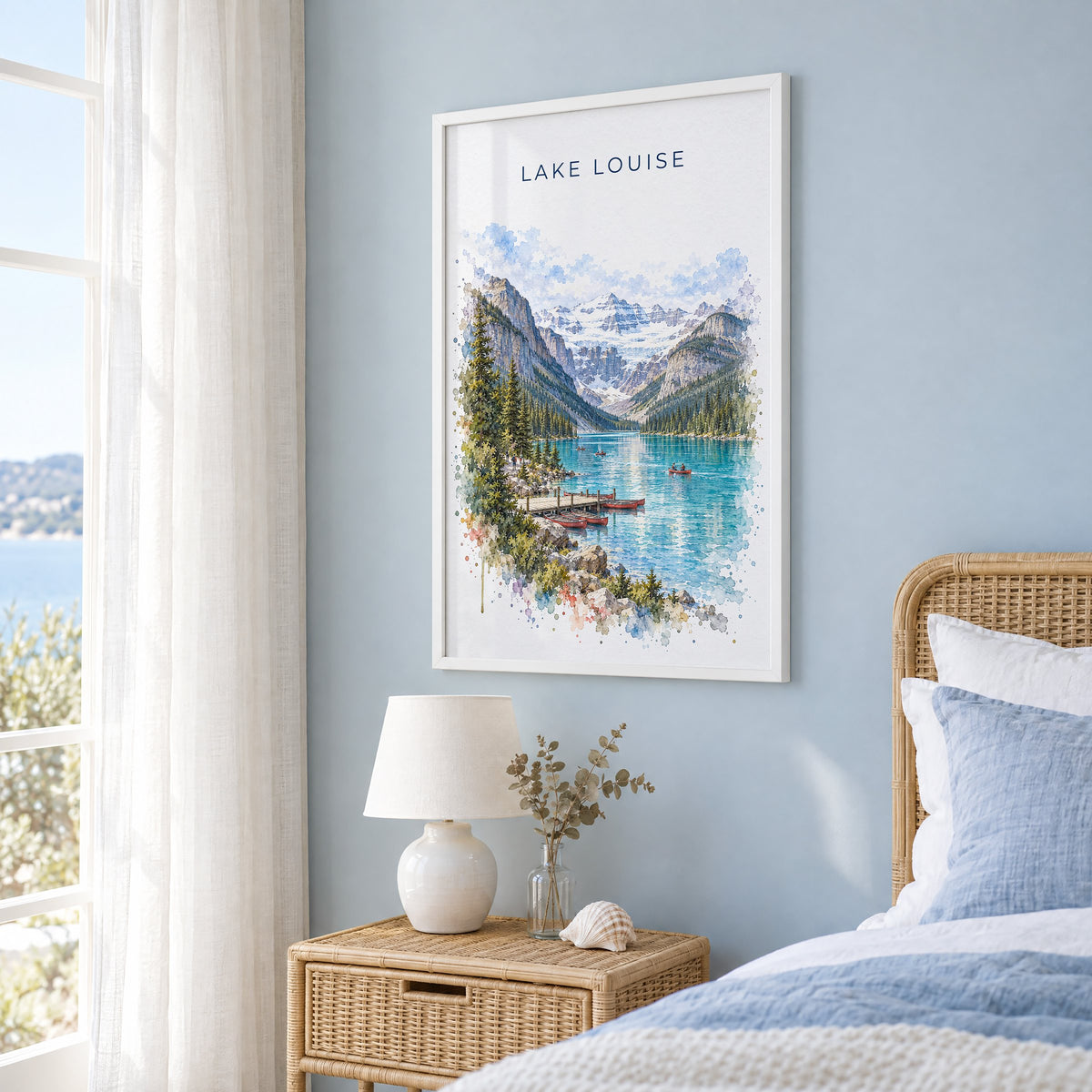 Lake Louise watercolor print in a white frame on a pale blue wall beside a rattan bed in a coastal bedroom