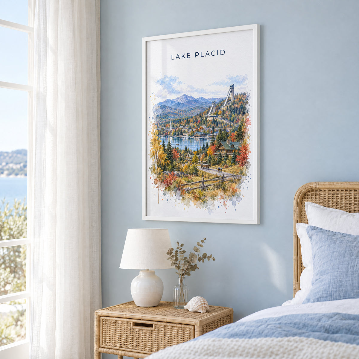Lake Placid watercolor print in a white frame on a pale blue wall beside a rattan bed in a coastal bedroom