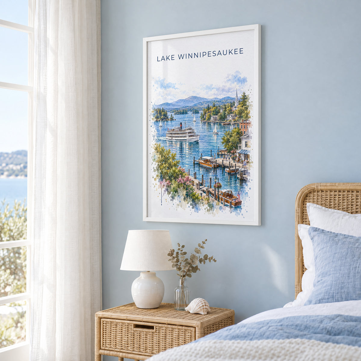 Lake Winnipesaukee watercolor print in a white frame on a pale blue wall beside a rattan bed in a coastal bedroom
