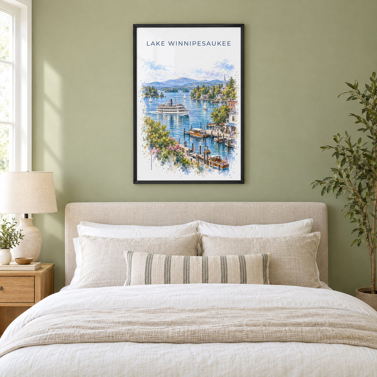 Lake Winnipesaukee watercolor print in a black frame above an upholstered headboard in a sage green bedroom