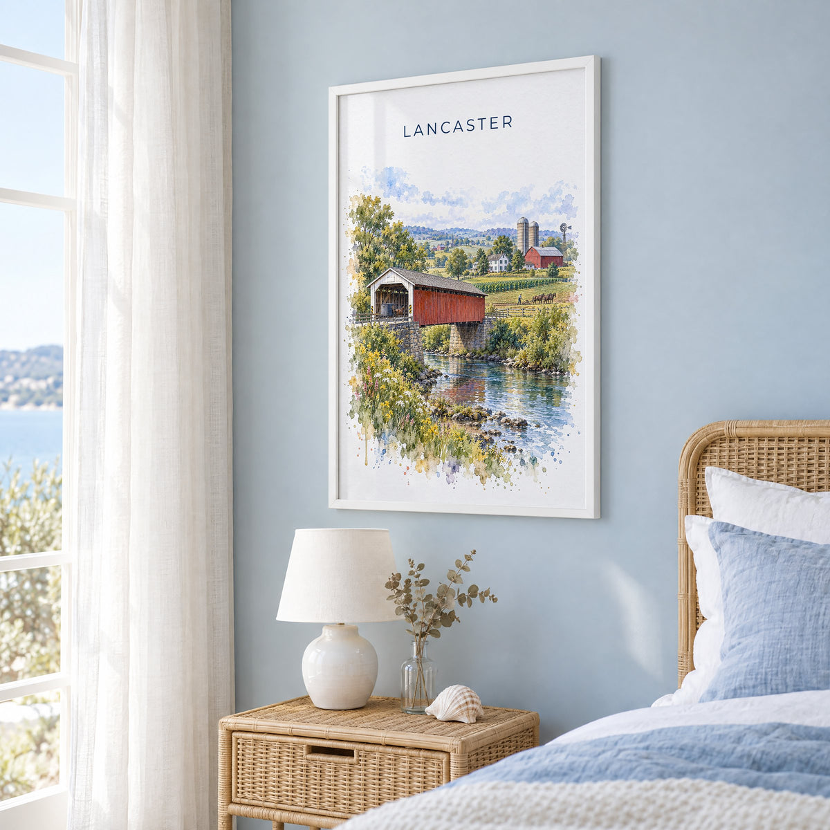 Lancaster, Pennsylvania watercolor print in a white frame on a pale blue wall beside a rattan bed in a coastal bedroom