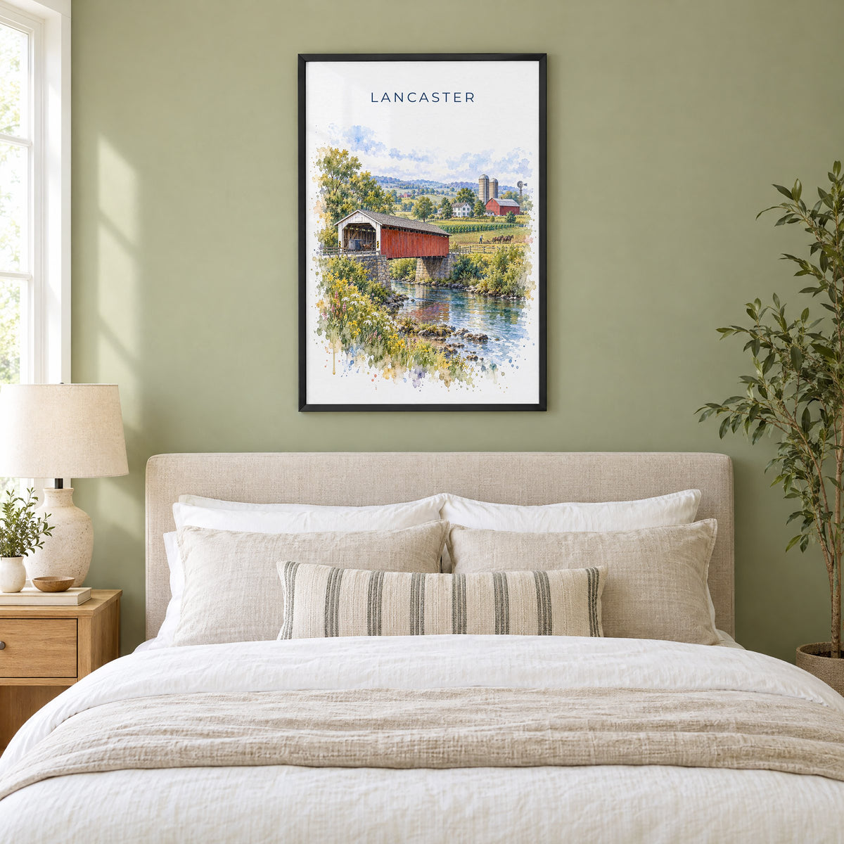 Lancaster, Pennsylvania watercolor print in a black frame above an upholstered headboard in a sage green bedroom