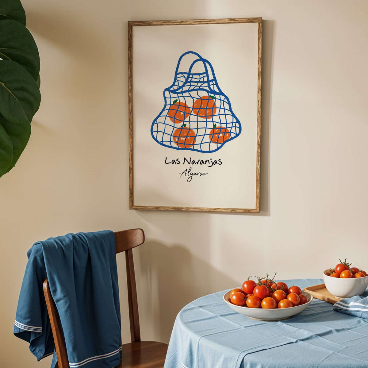 Las naranjas orange net bag print in an oak frame above a blue linen table with tomatoes