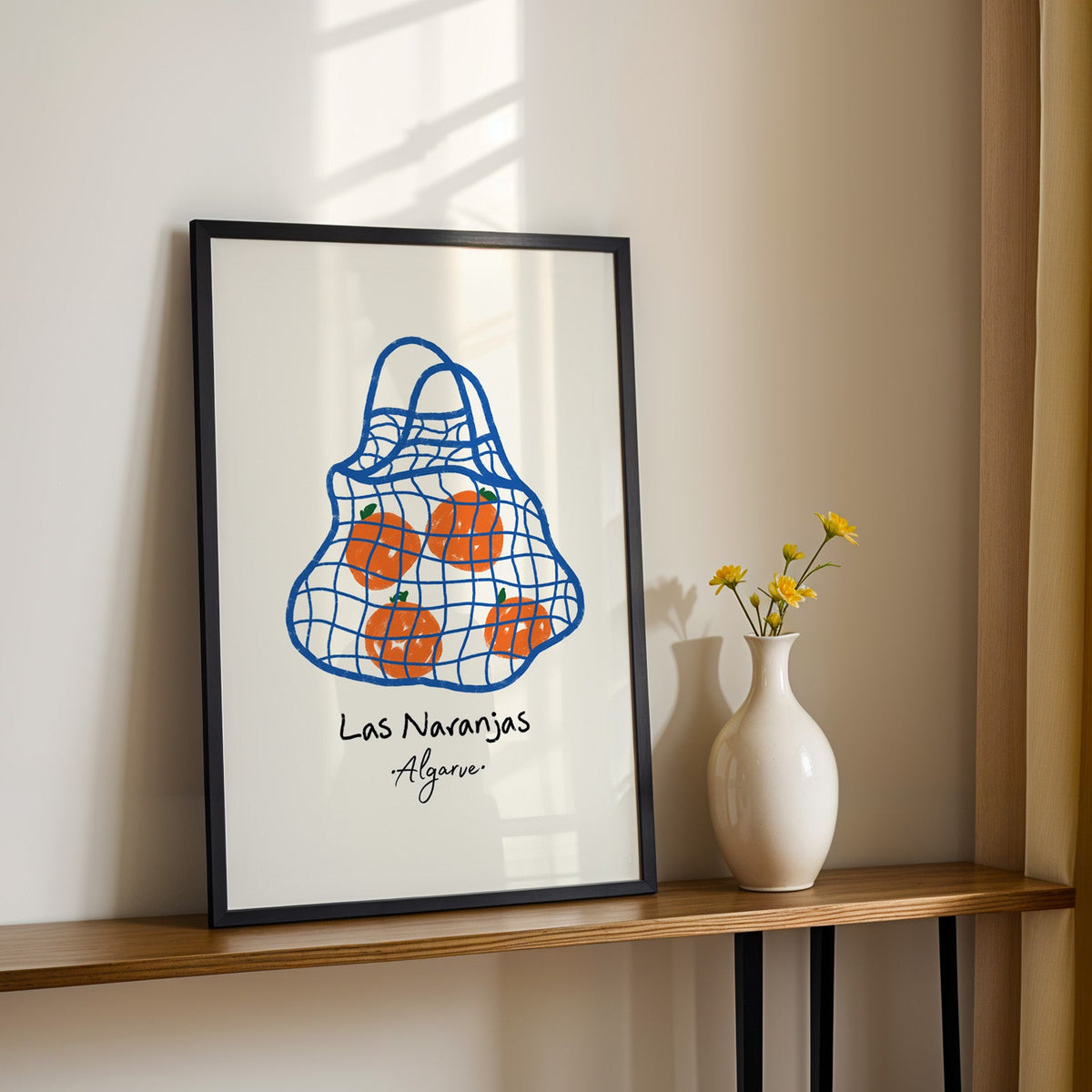 Las naranjas orange net bag print in a black frame on a console table with daisies