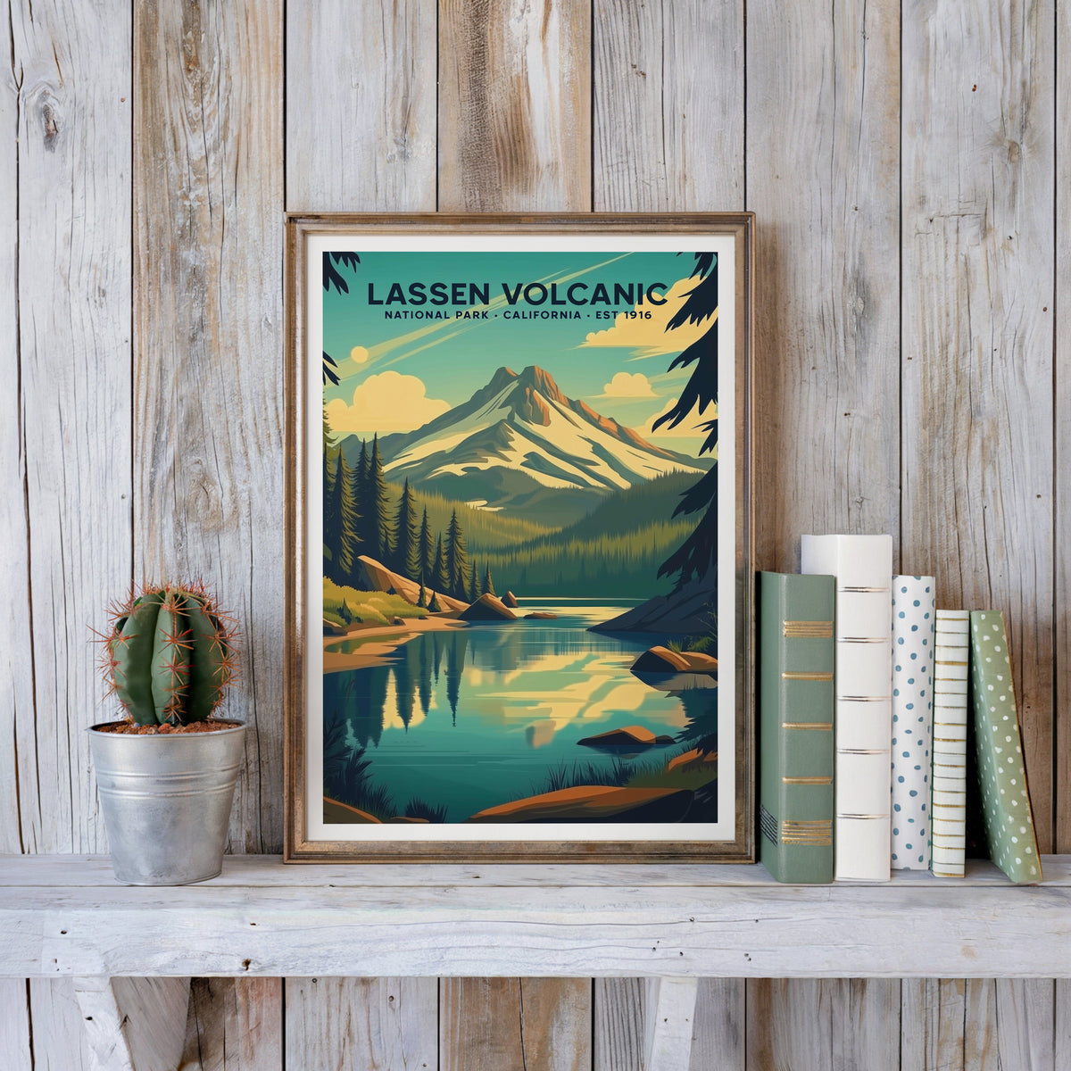 Lassen Volcanic poster in an antique gold frame against whitewashed planks beside books and a cactus