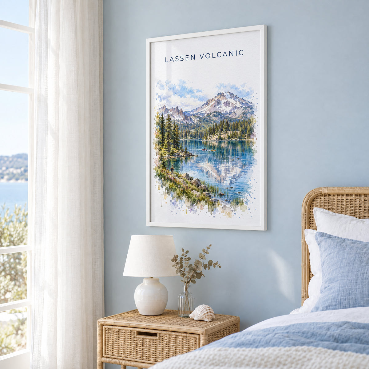 Lassen Volcanic National Park watercolor print in a white frame on a pale blue wall beside a rattan bed in a coastal bedroom