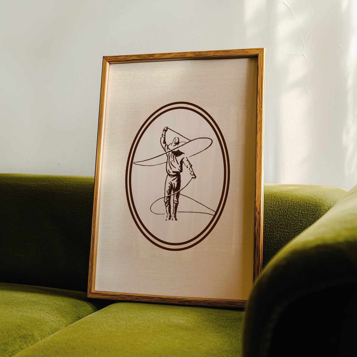 Lasso cowboy oval print in an oak frame leaning on a green velvet sofa