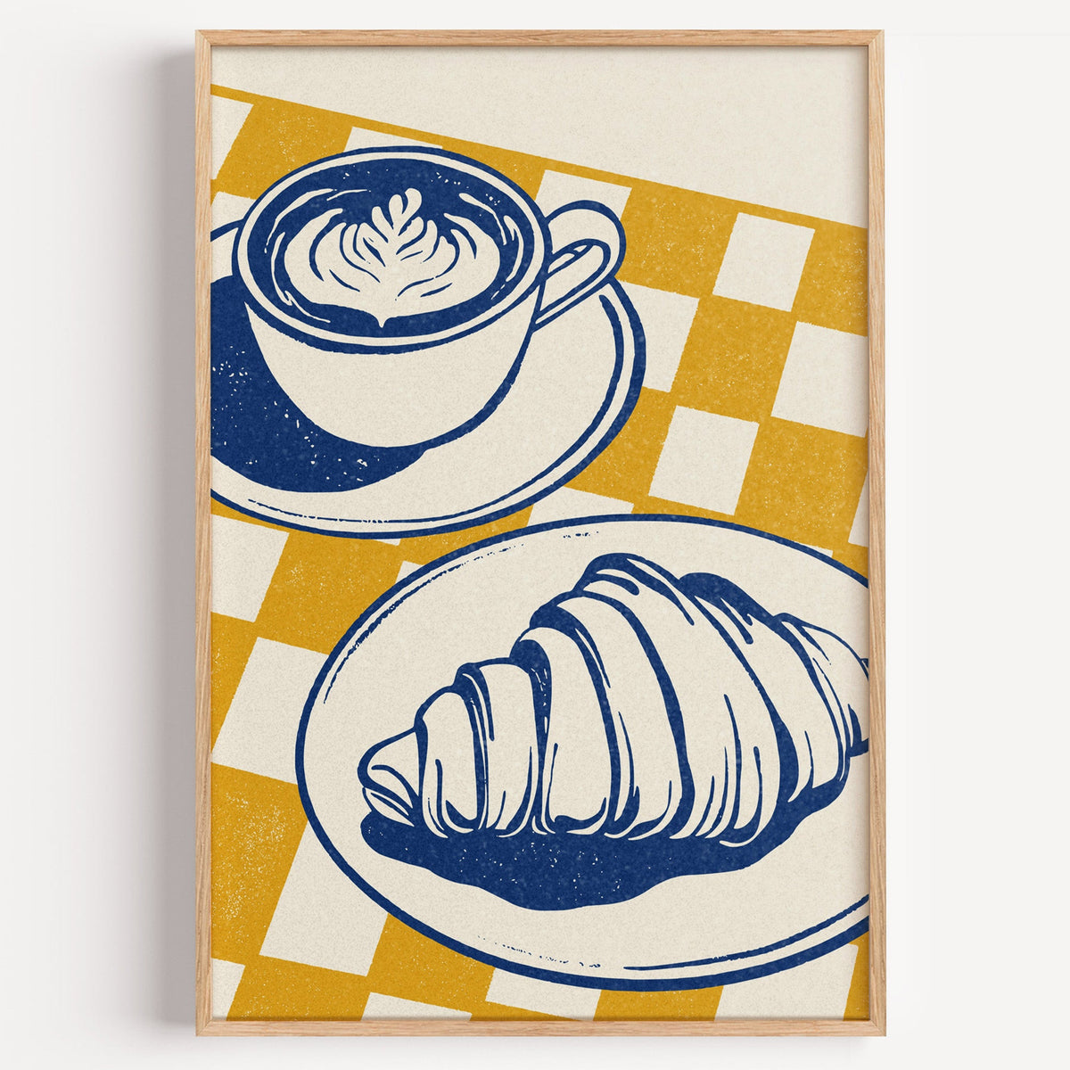 Latte and croissant block print in a light oak frame on a plain white wall