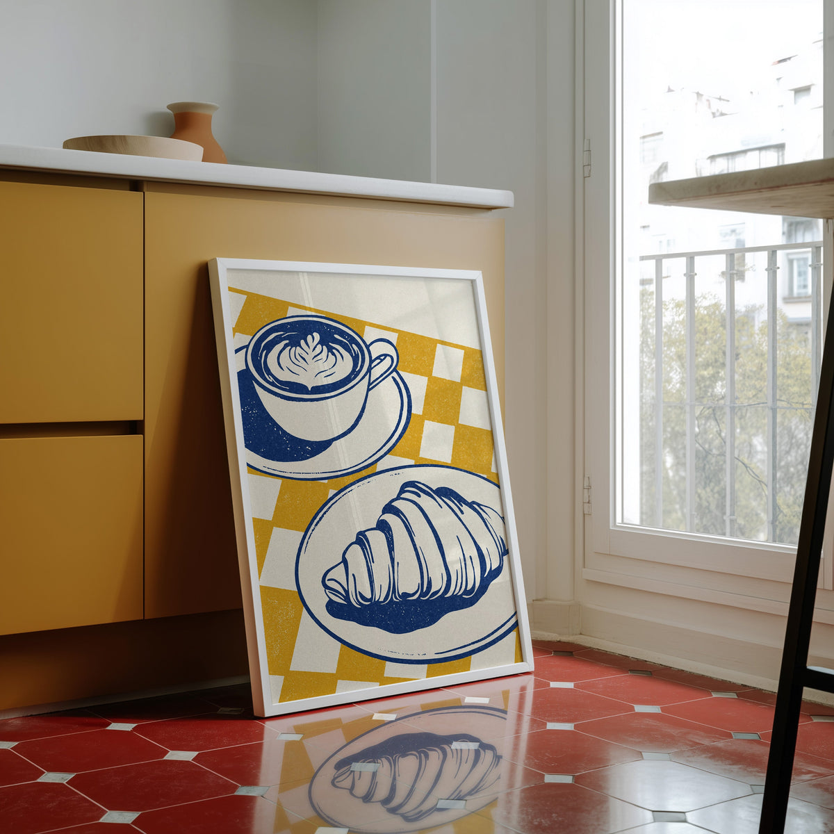Latte and croissant print in a white frame against yellow cabinets on a red tiled floor