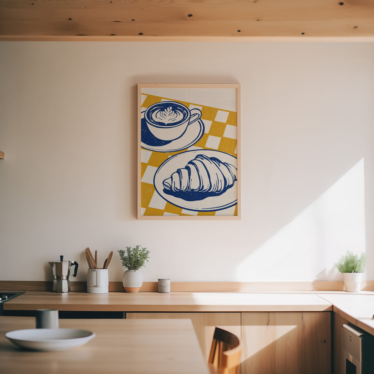 Latte and croissant print in an oak frame above a wood counter with a moka pot and herbs