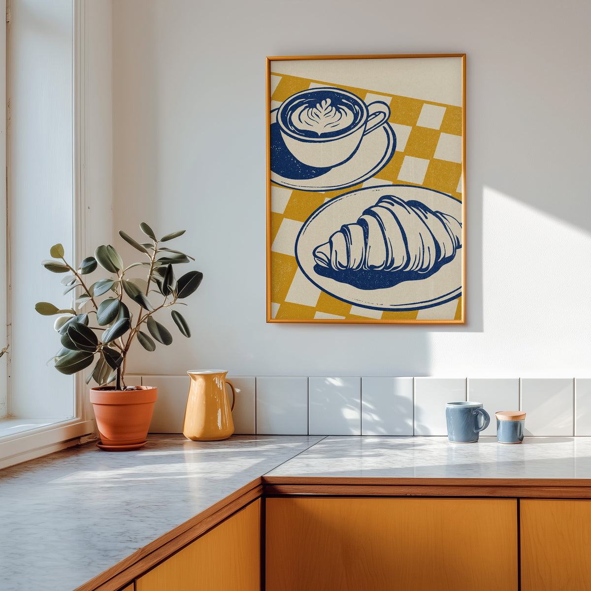 Latte and croissant print shown in a gold frame above a marble counter with a yellow ceramic jug