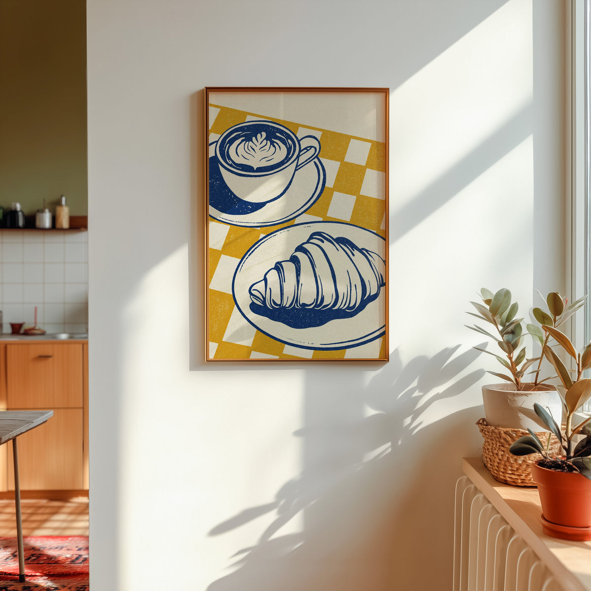 Latte and croissant print shown in a gold frame in sunlight with plants and a kitchen beyond