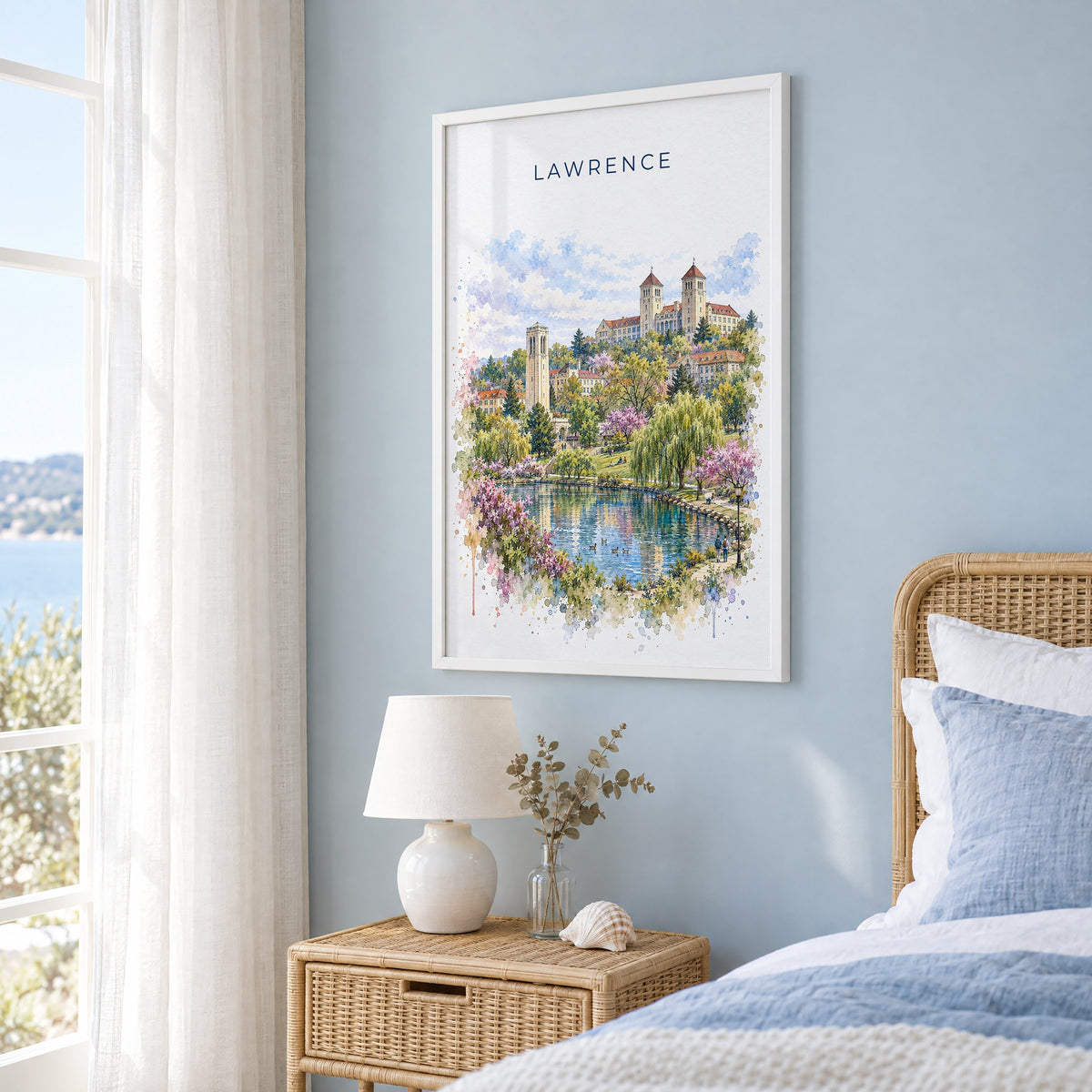 Lawrence, Kansas watercolor print in a white frame on a pale blue wall beside a rattan bed in a coastal bedroom