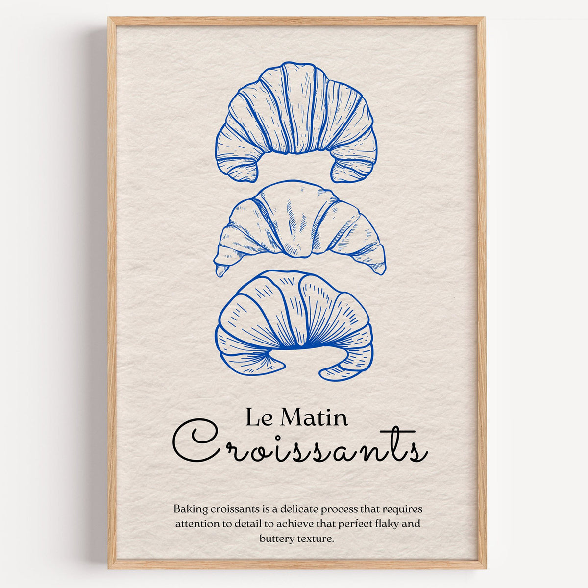 Le Matin Croissants cobalt engraving print in a light oak frame on a plain white wall