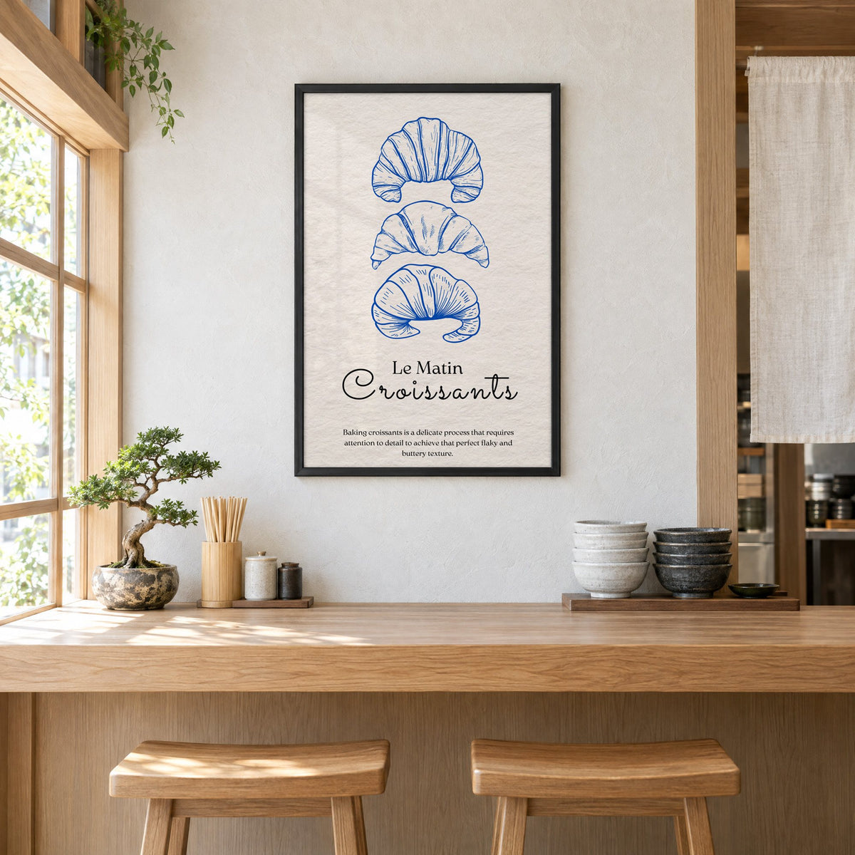 Le Matin Croissants cobalt engraving print in a black frame above a light wood ramen counter with stools and stacked bowls