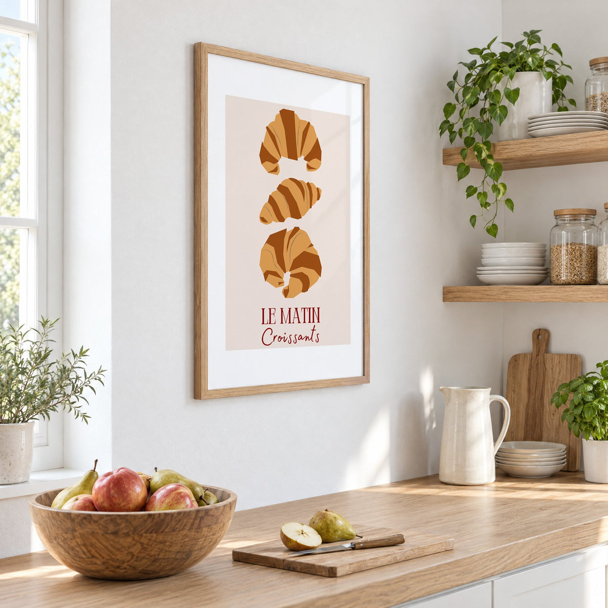 LE MATIN Croissants caramel trio print in an oak frame on a white kitchen wall above a counter with apples and pears, seen at an angle
