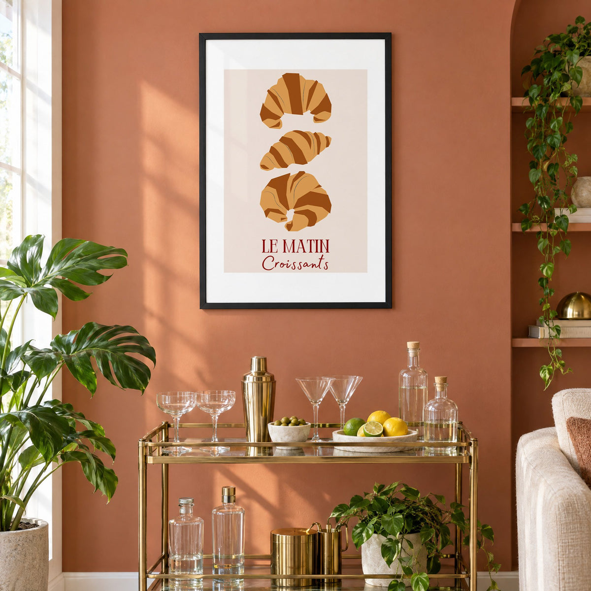LE MATIN Croissants caramel trio print in a black frame on a terracotta wall above a brass bar cart with coupes and citrus