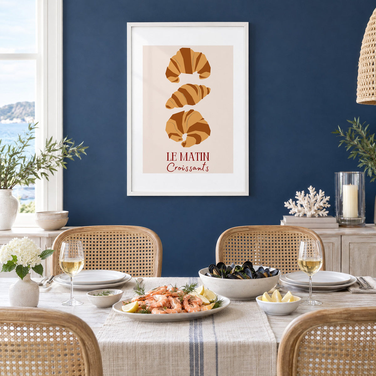 LE MATIN Croissants caramel trio print in a white frame on a navy wall above a dining table set with shrimp and mussels