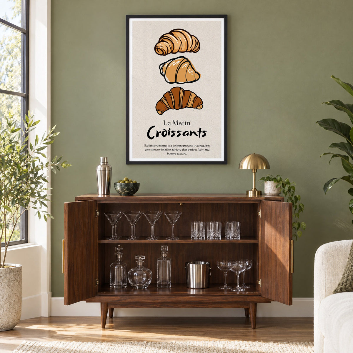 Le Matin Croissants three croissants print in a black frame on an olive green wall above a walnut bar cabinet with glassware