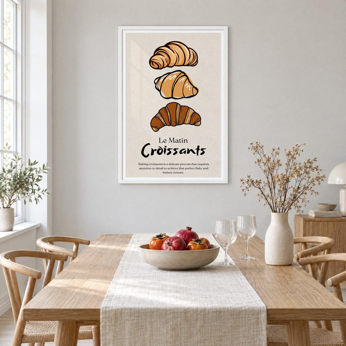 Le Matin Croissants three croissants print in a white frame above a light oak dining table with a linen runner and fruit bowl