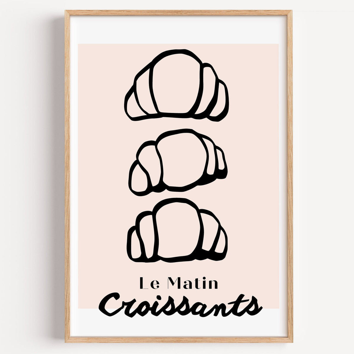 Le Matin black outline croissants print in a light oak frame on a plain white wall