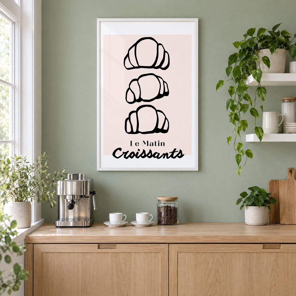 Le Matin black outline croissants print in a white frame on a sage green coffee nook wall above an espresso machine