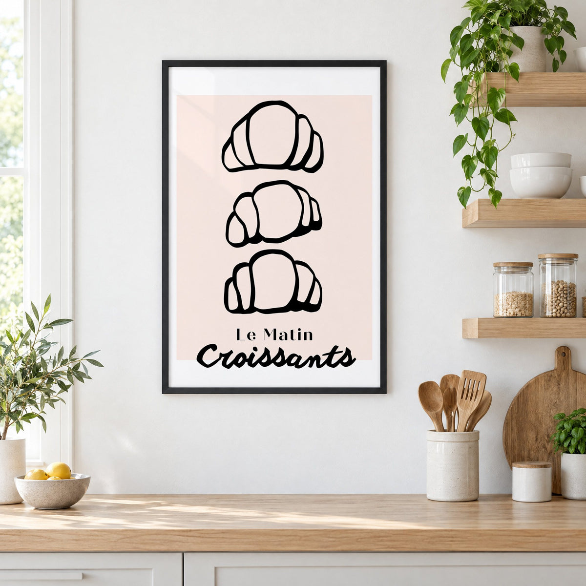 Le Matin black outline croissants print in a black frame in a white kitchen beside open wood shelves and glass jars