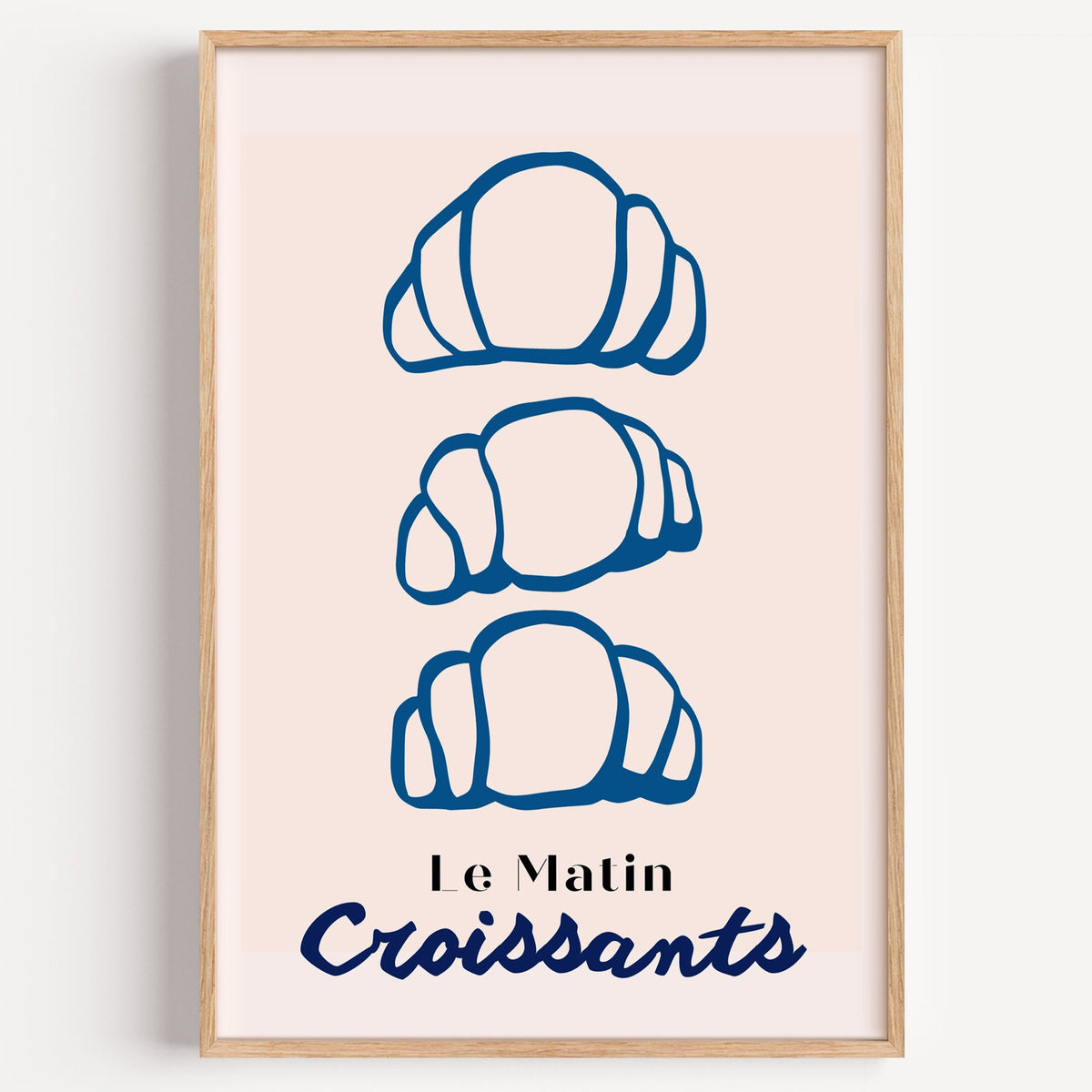 Le Matin blue croissants print in a light oak frame on a plain white wall