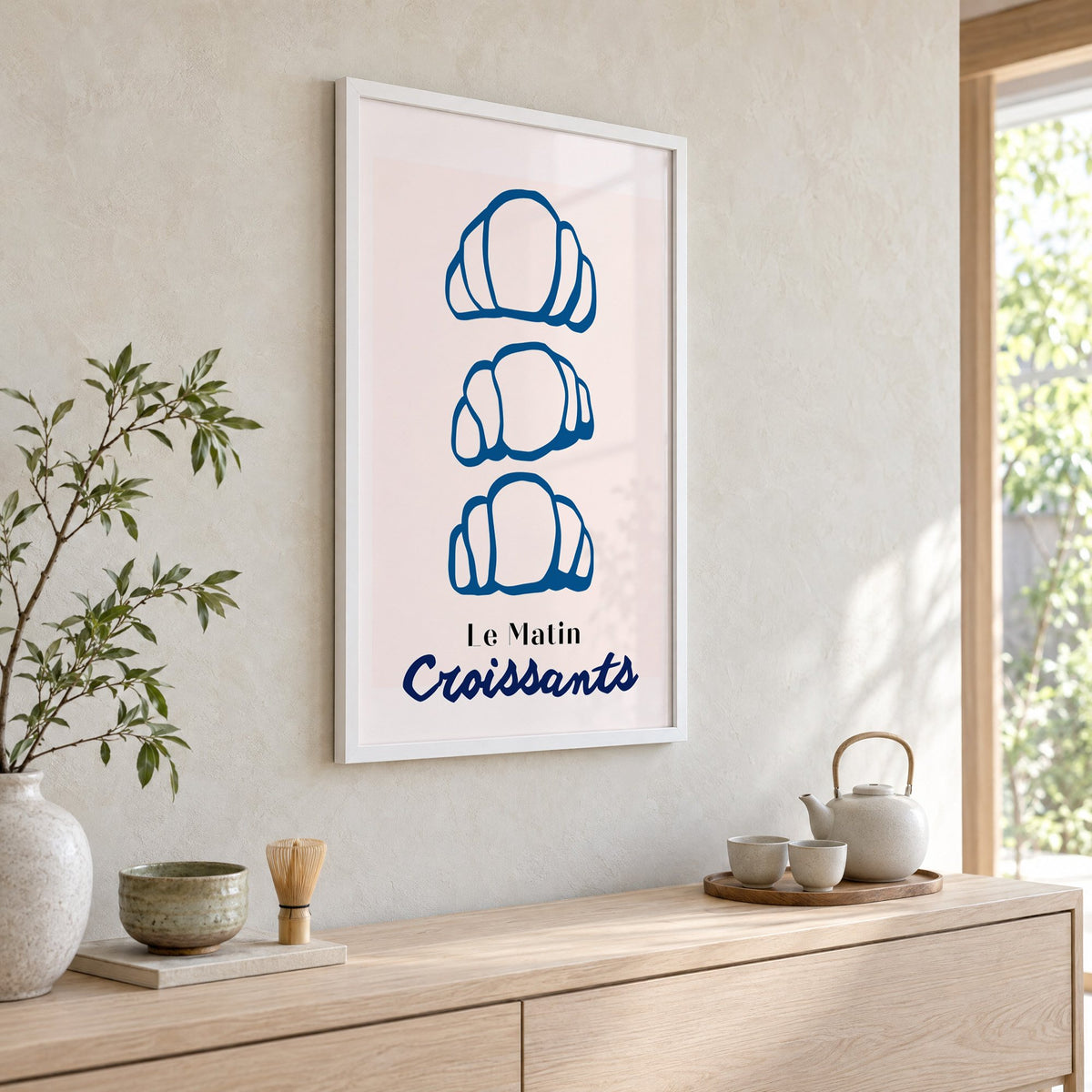 Le Matin blue croissants print in a white frame above a pale wood console with a matcha tea set