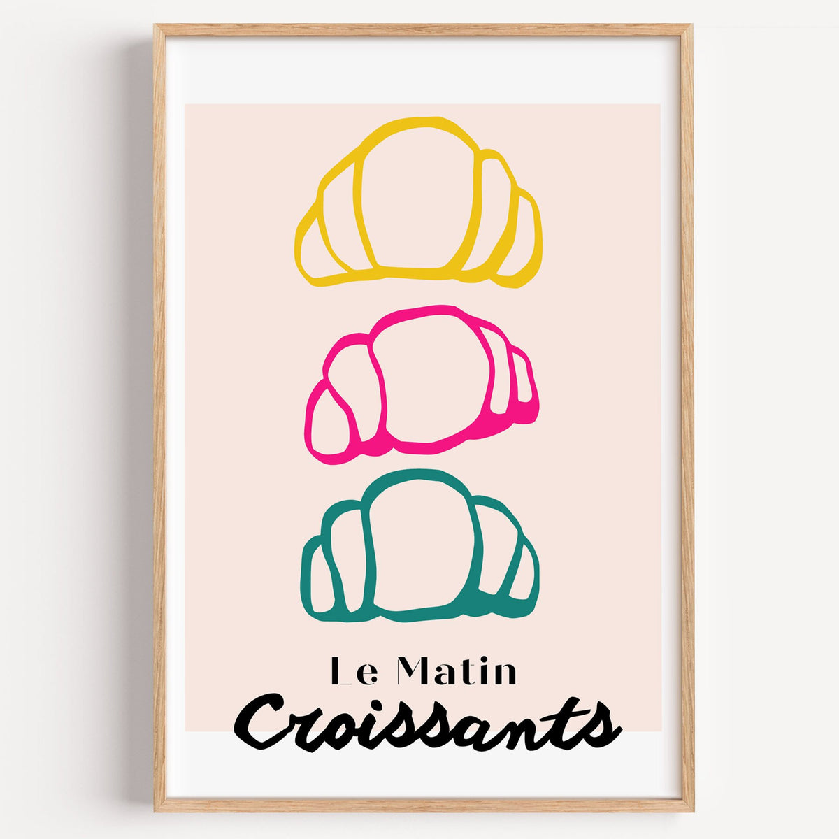 Le Matin colorful croissants print in a light oak frame on a plain white wall