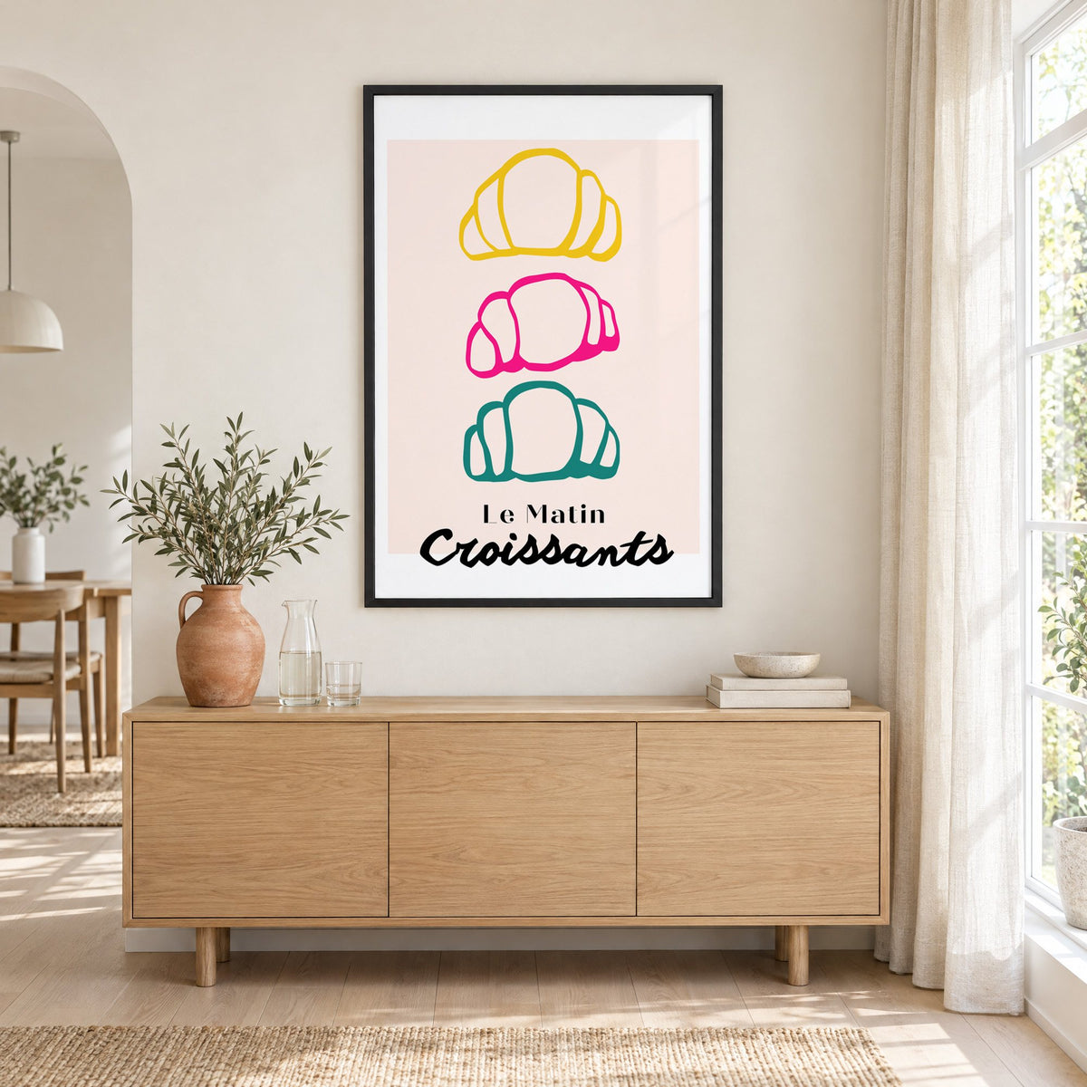 Le Matin colorful croissants print in a black frame above an oak sideboard with a terracotta vase of olive branches