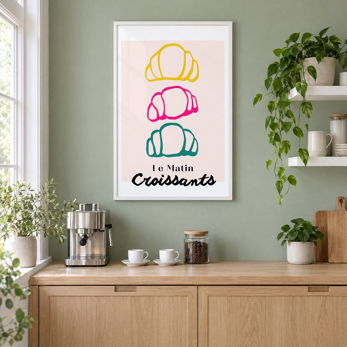 Le Matin colorful croissants print in a white frame on a sage green coffee nook wall above an espresso machine