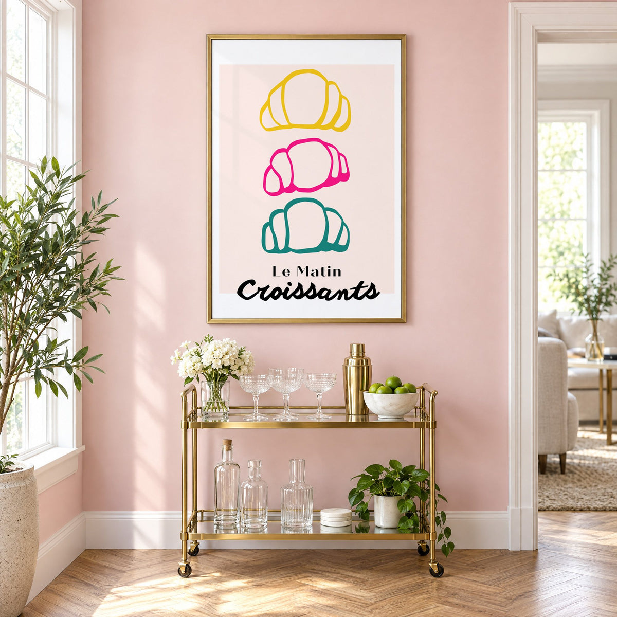 Le Matin colorful croissants print in a brass frame above a gold bar cart on a blush pink wall