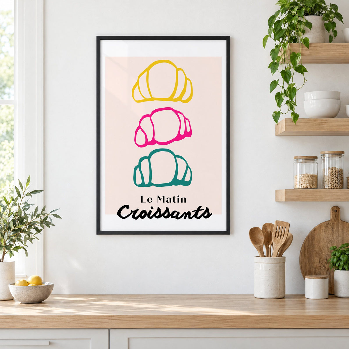 Le Matin colorful croissants print in a black frame in a white kitchen beside open wood shelves and glass jars