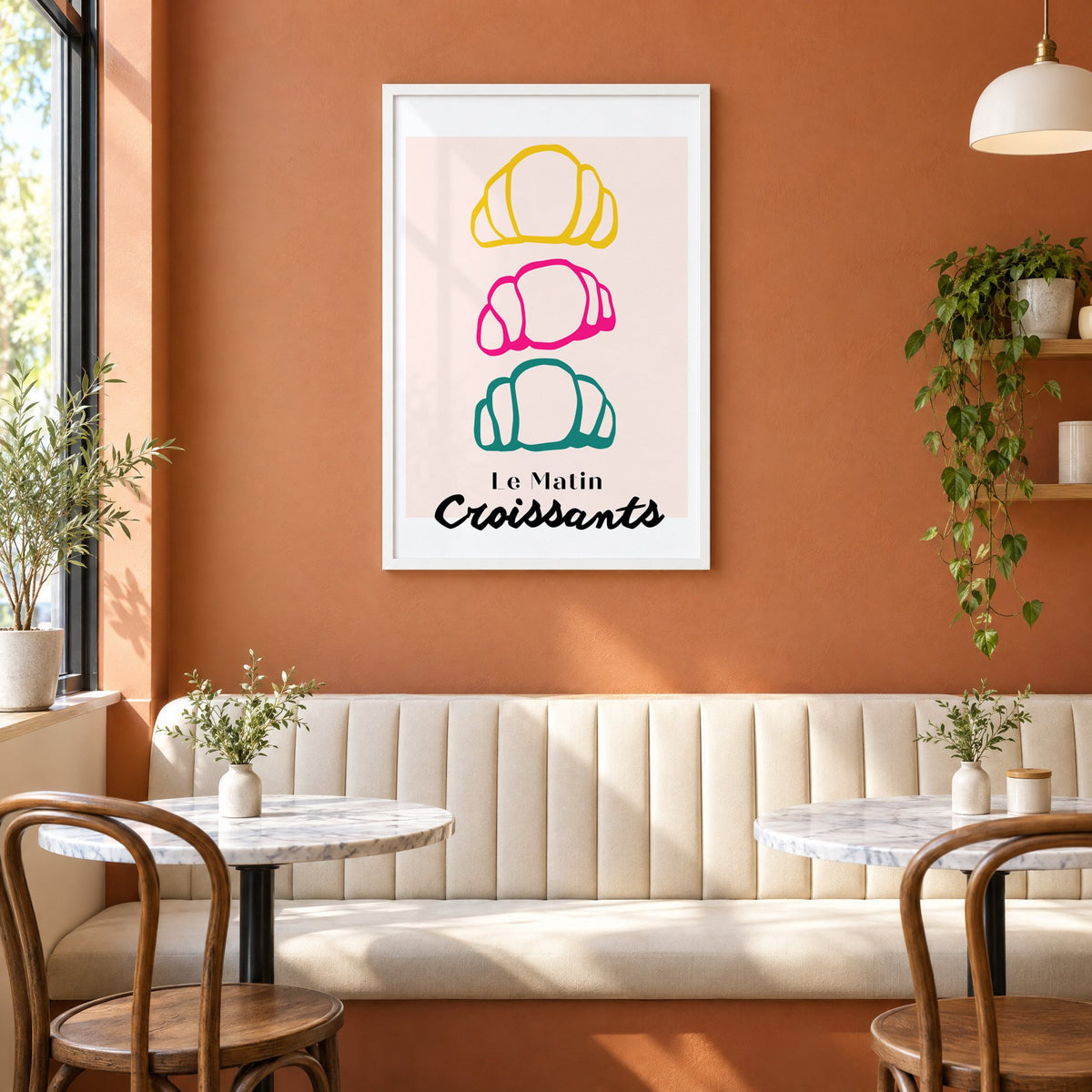 Le Matin colorful croissants print in a white frame above a cream banquette on a terracotta cafe wall