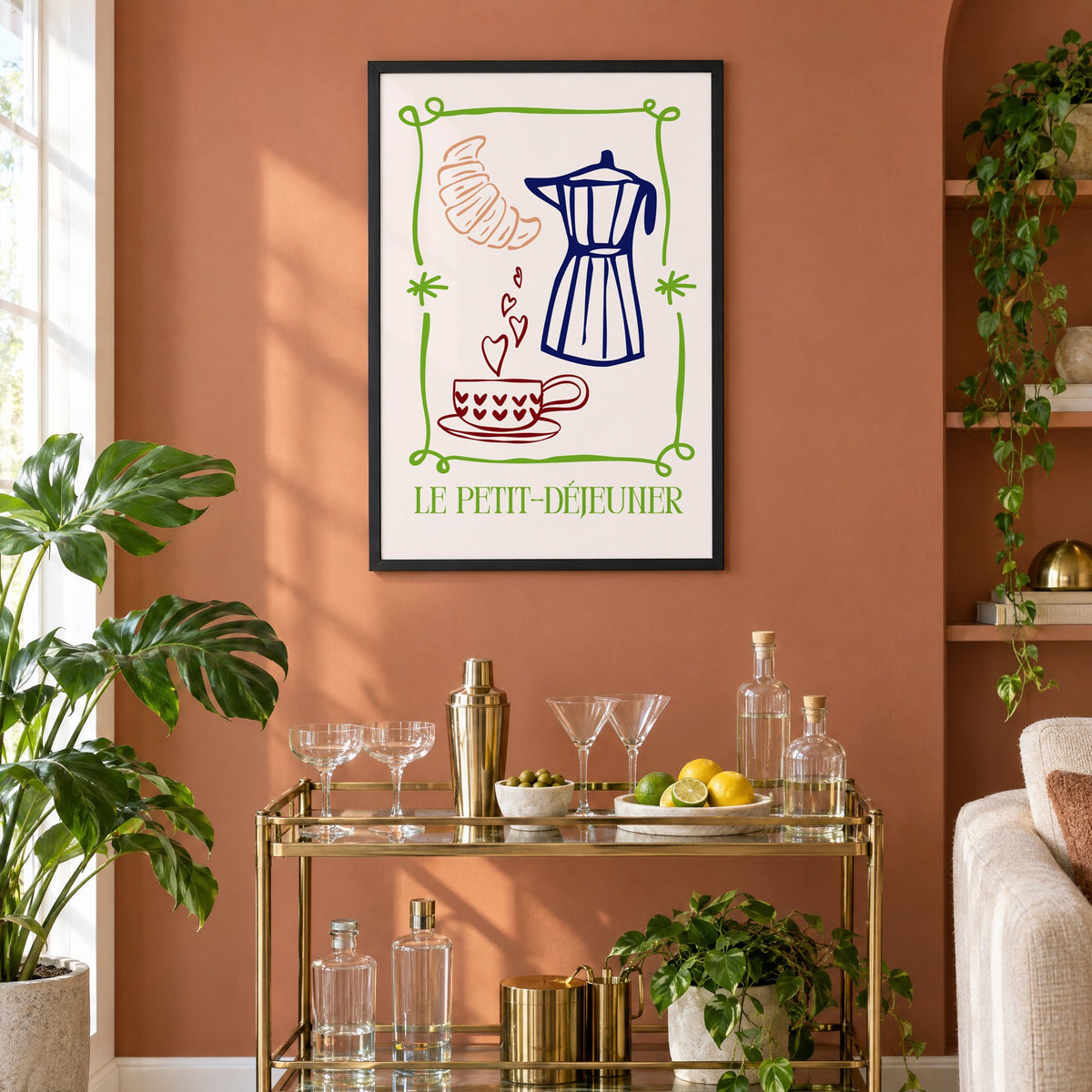 LE PETIT-DÉJEUNER moka pot and croissant print in a black frame on a terracotta wall above a brass bar cart with coupes and citrus