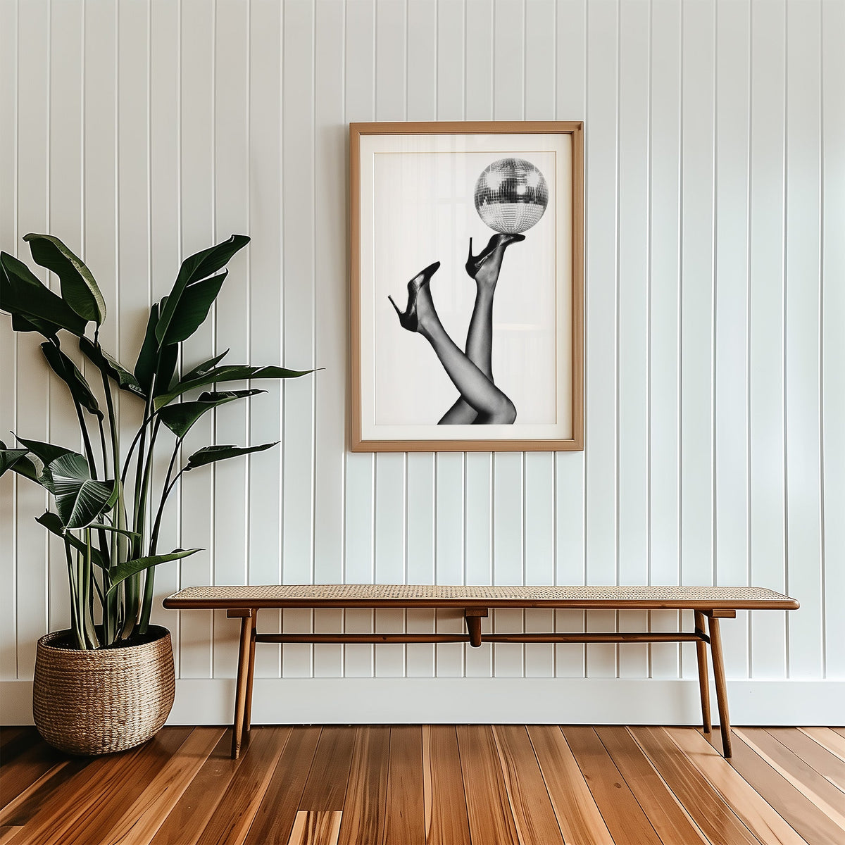 Legs in heels balancing a disco ball print in a wood frame with a white mat above a cane bench