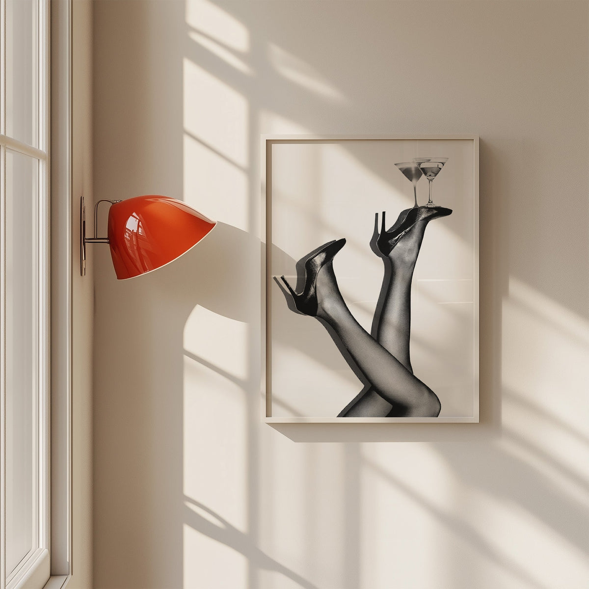 Legs in heels balancing two martini glasses print in a white frame on a sunlit wall beside a red sconce