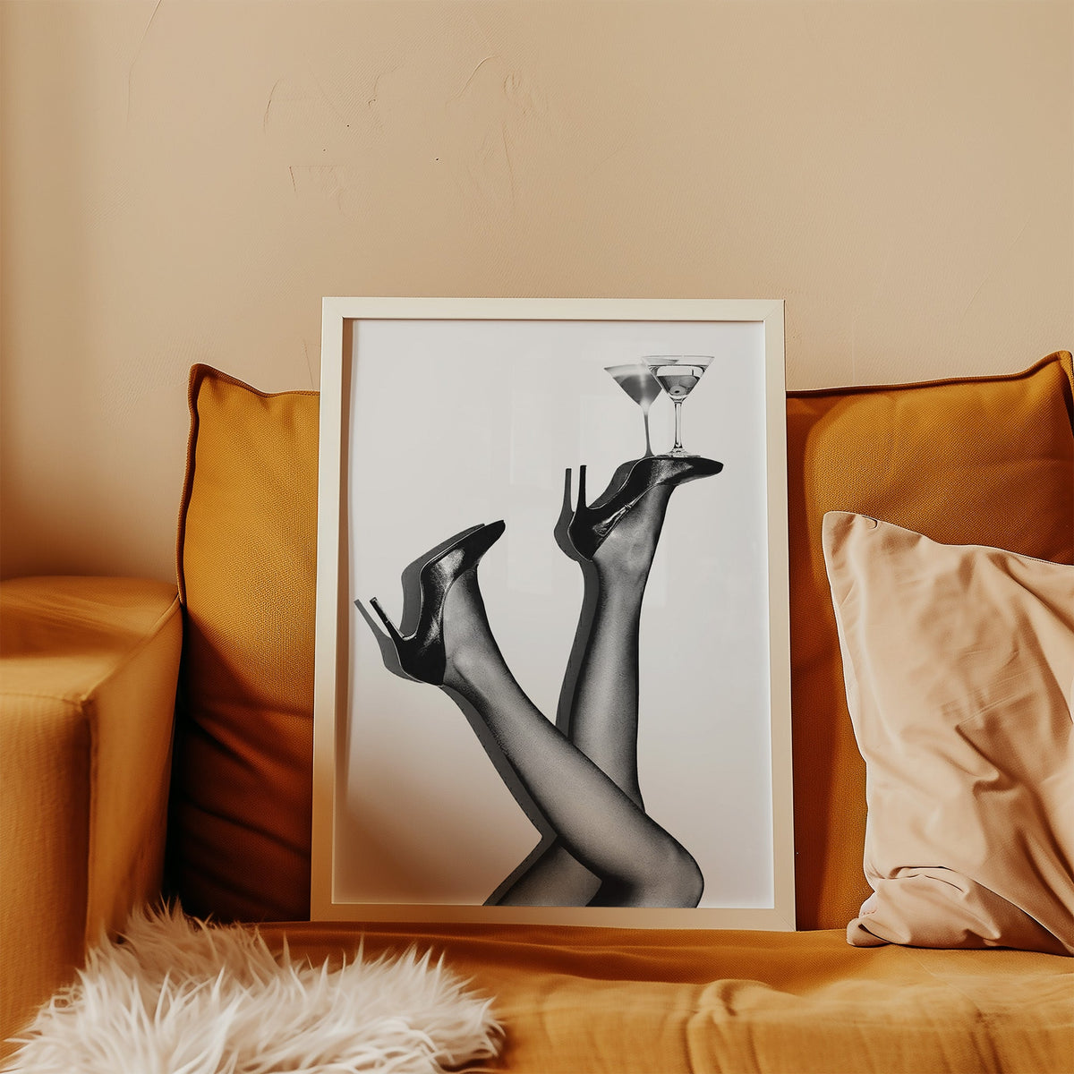 Legs in heels balancing two martini glasses print in a white frame leaning on a mustard velvet sofa