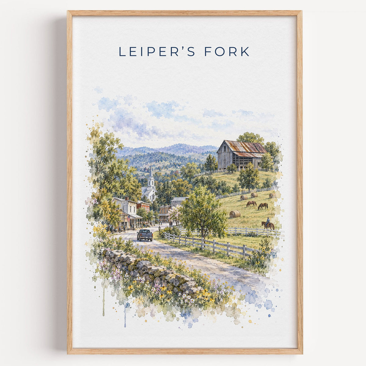 Leiper's Fork, Tennessee watercolor print in a light oak frame on a plain white wall