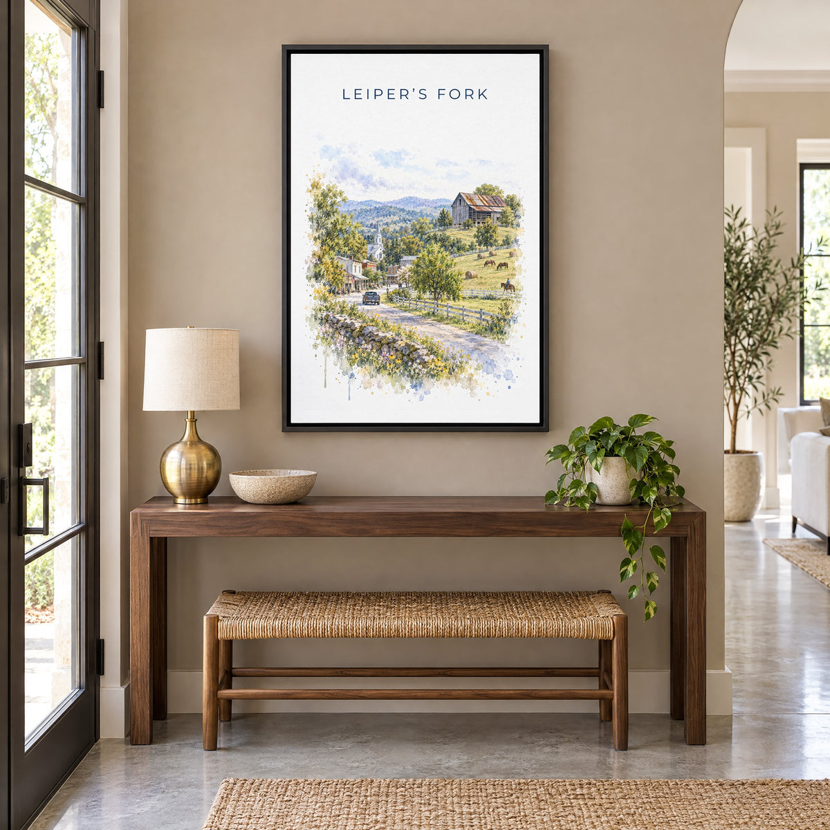 Leiper's Fork, Tennessee watercolor print as a black floater canvas above a walnut console and woven bench in an entryway